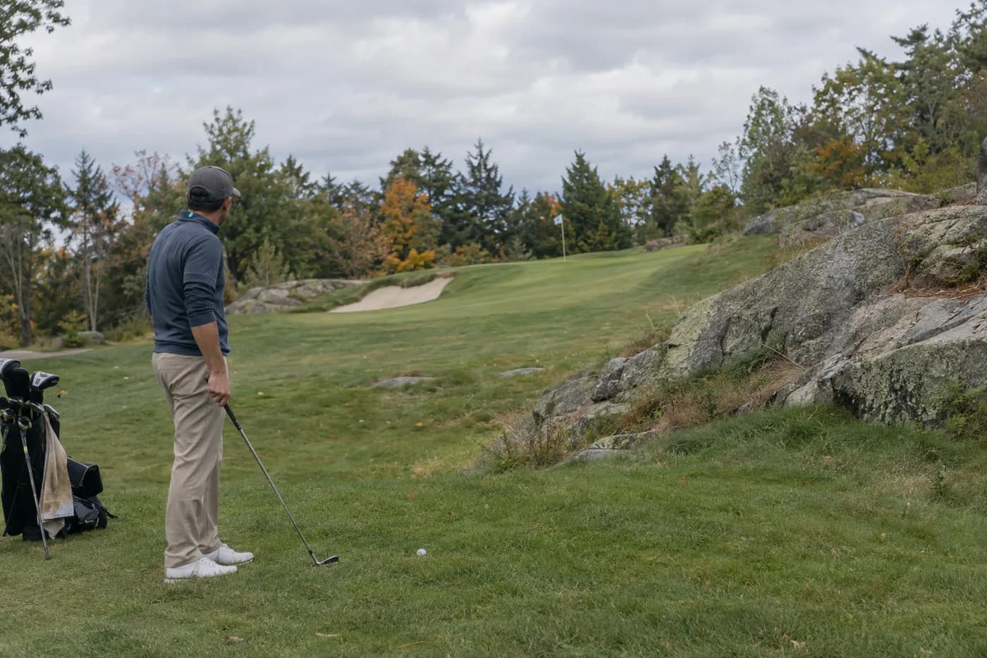 a golfer studying an uphill approach beside a granite ledge