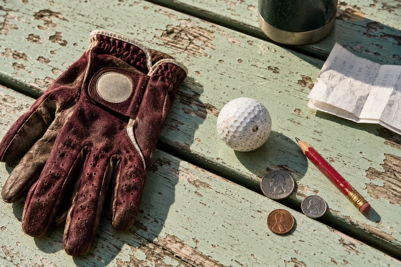 A scuffed golf ball, coins and a pencil on a folded receipt