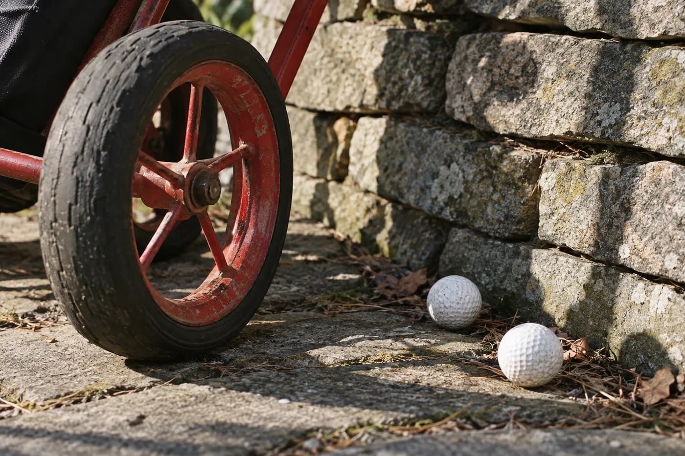 a red push-cart wheel and two golf balls beside a stone wall
