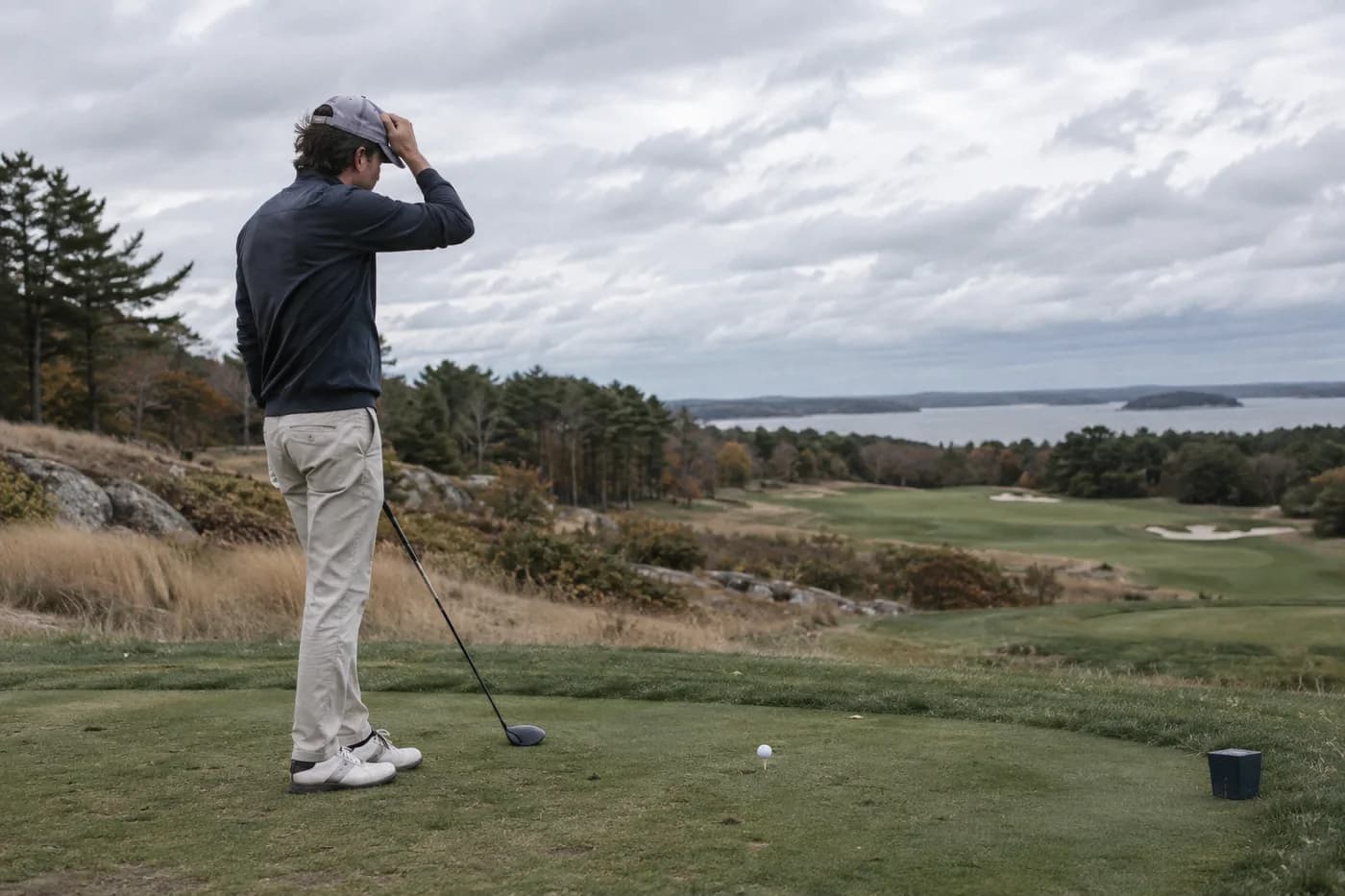 a golfer holding a cap against a crosswind on an exposed tee