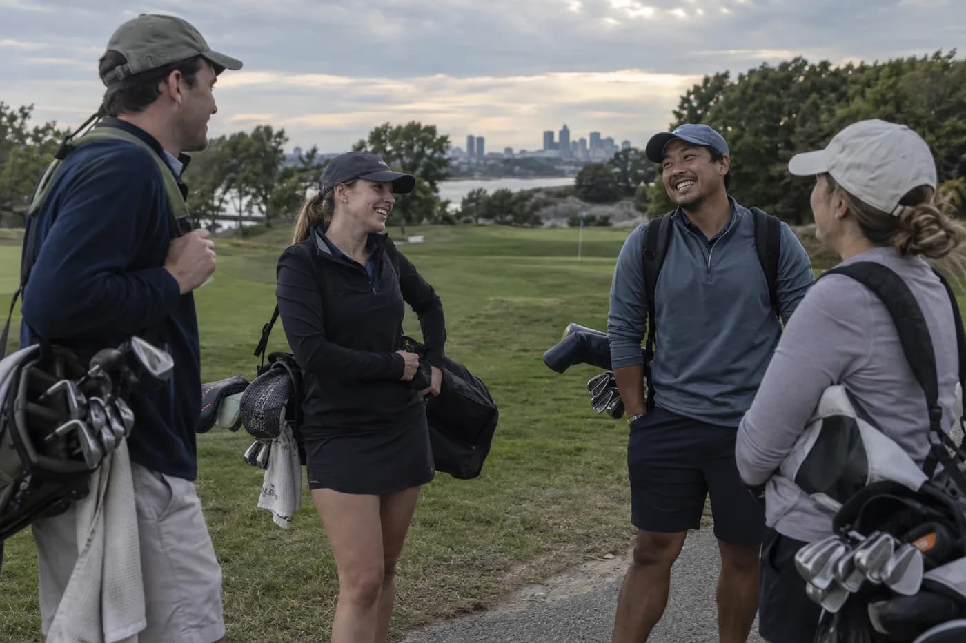 a mixed group of adult golfers chatting beside bags at the end of an evening round