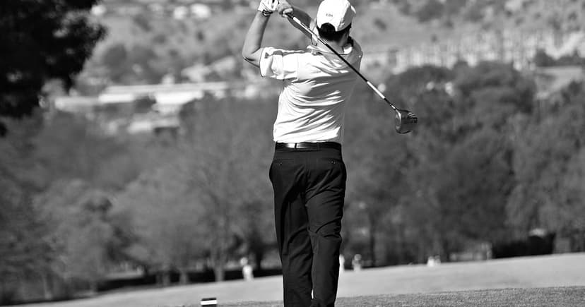 Golfer completing a swing on a fairway, black and white