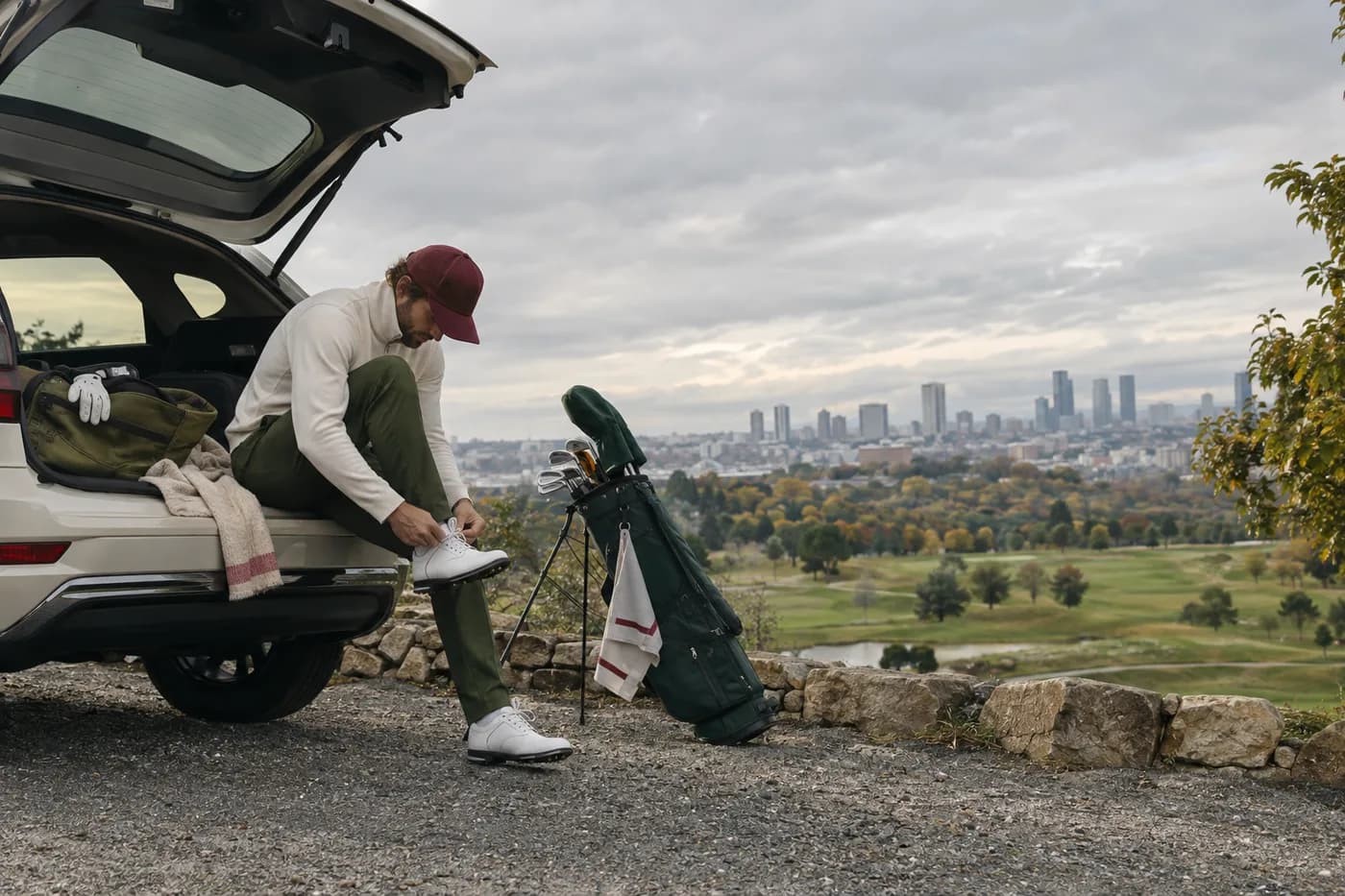 a golfer tying shoes beside a car with the city in the distance