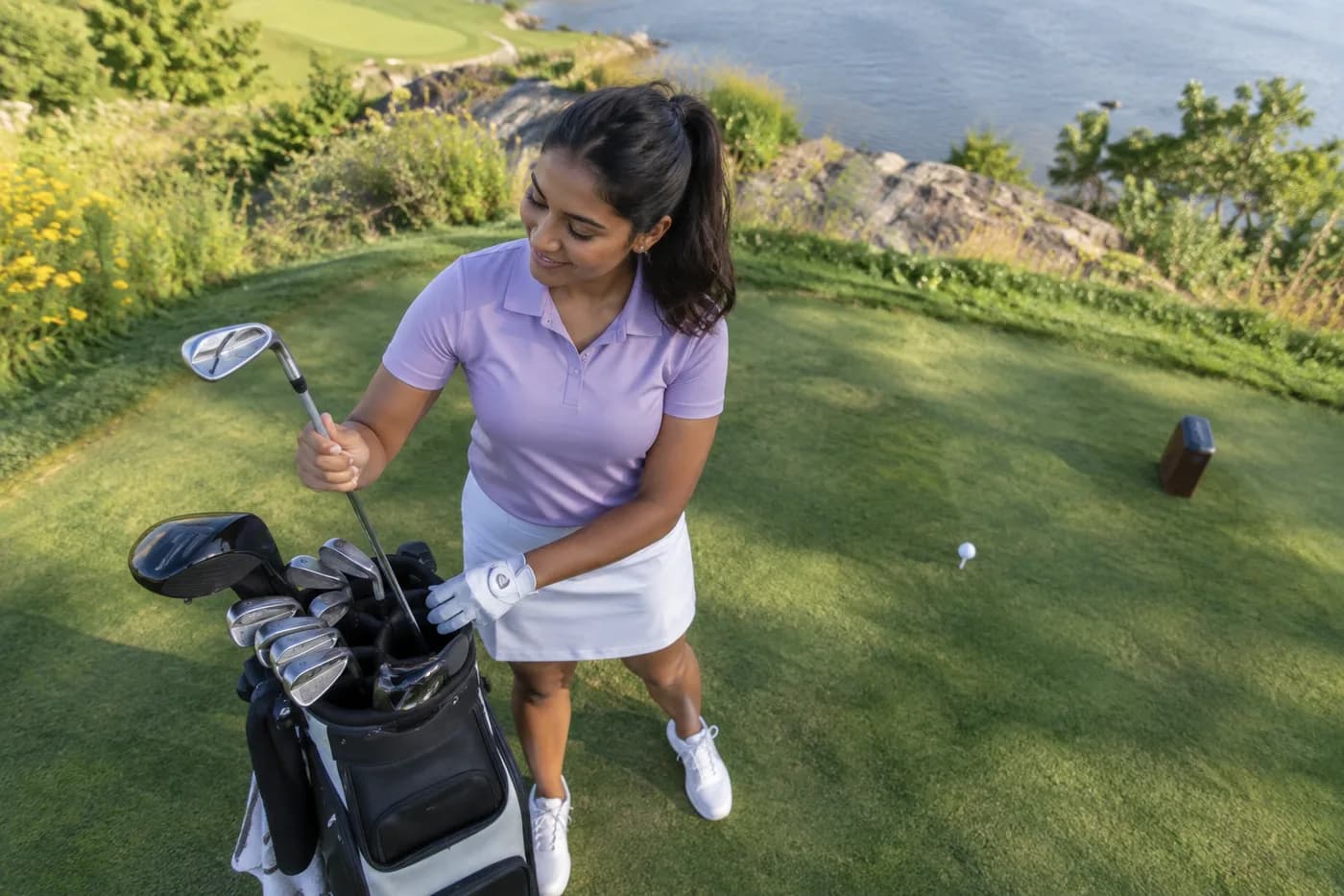 a golfer in a lavender polo leaving driver in the bag while pulling an iron at a short tight tee
