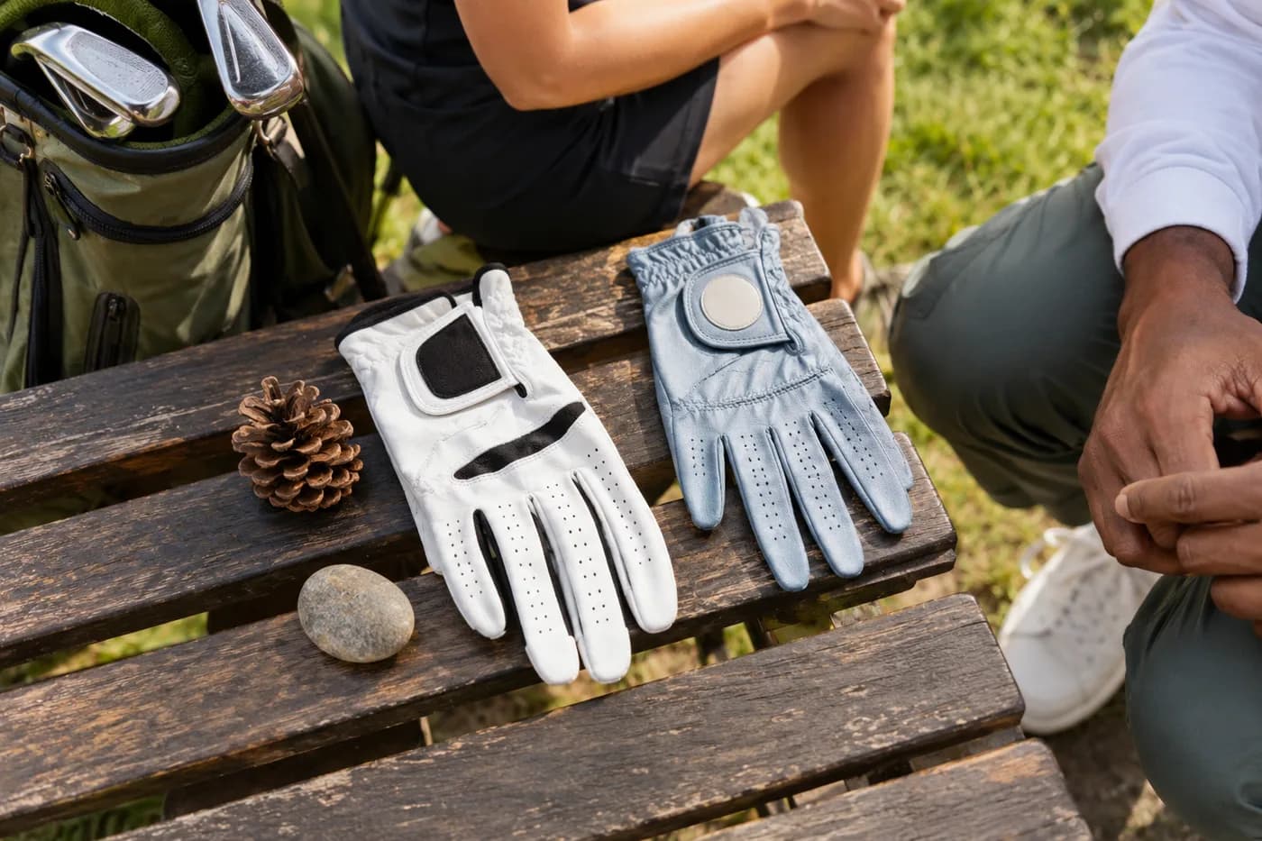 two different golf gloves on a bench with a pine cone and a small smooth river stone