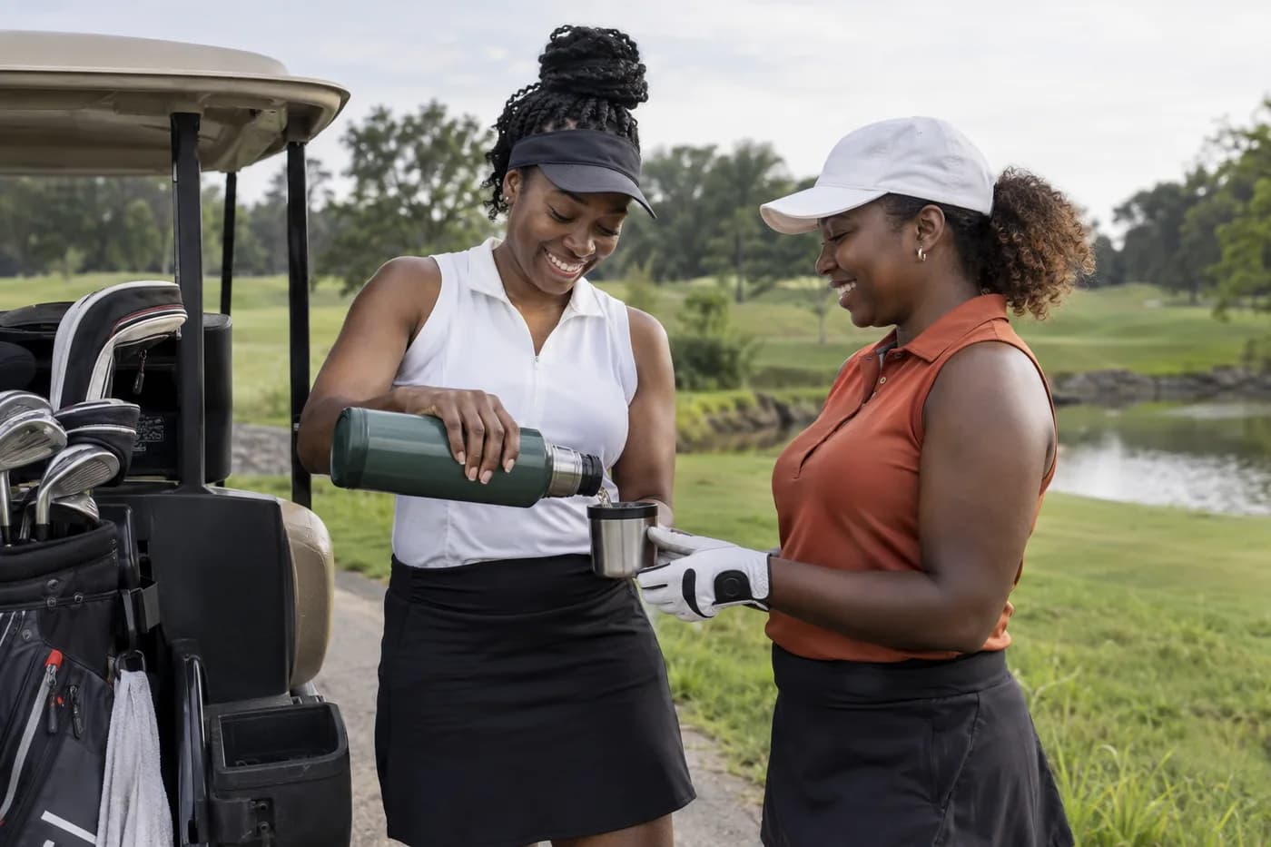 two golfers pouring coffee from a thermos beside clubs before a longer drive