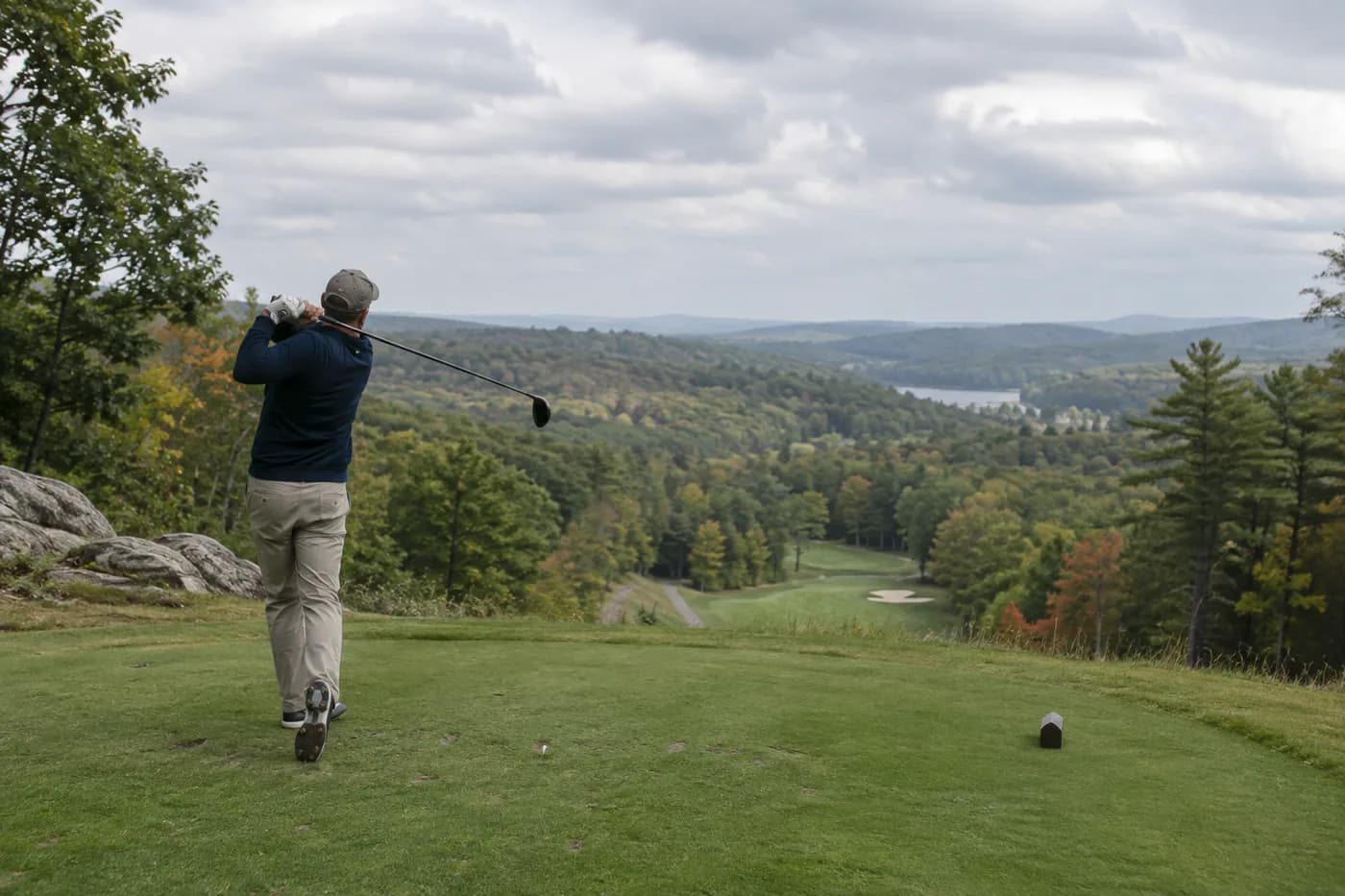 a golfer standing on an elevated tee looking into a broad wooded valley