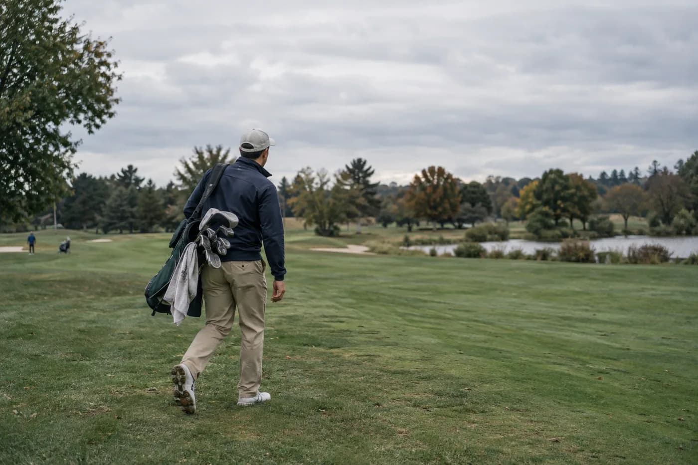 a golfer walking across an open parkland fairway with a small carry bag