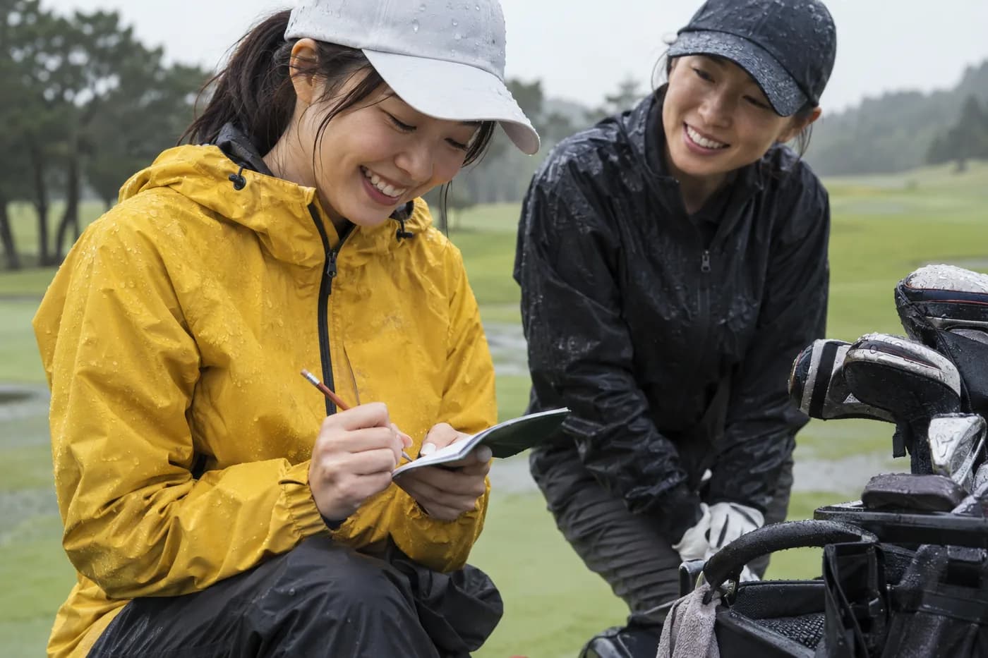 a golfer in a yellow rain jacket noting a score with pencil while a playing partner looks on